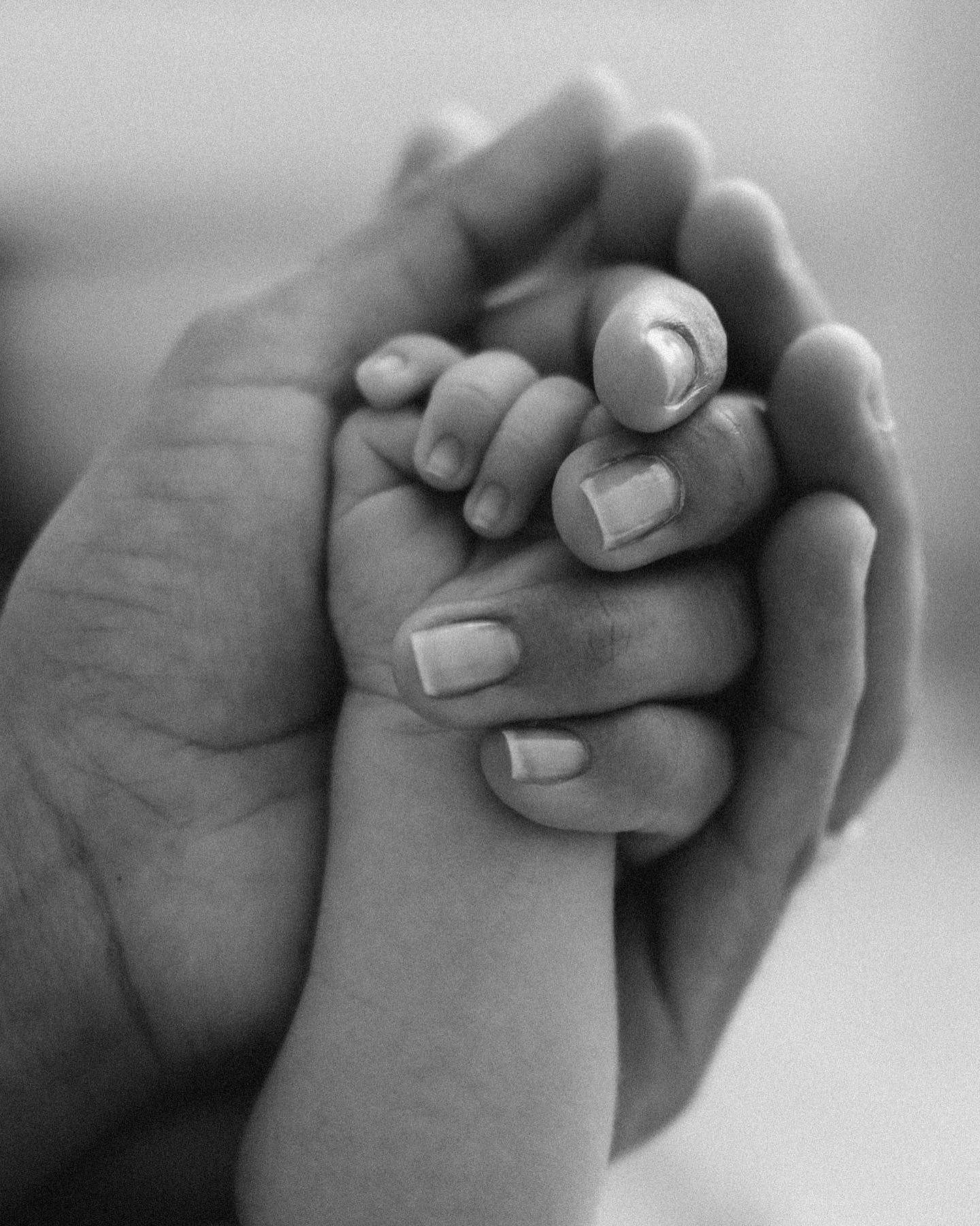 A black and white photo showing a baby and a woman holding hands, representing a bond of care and warmth.