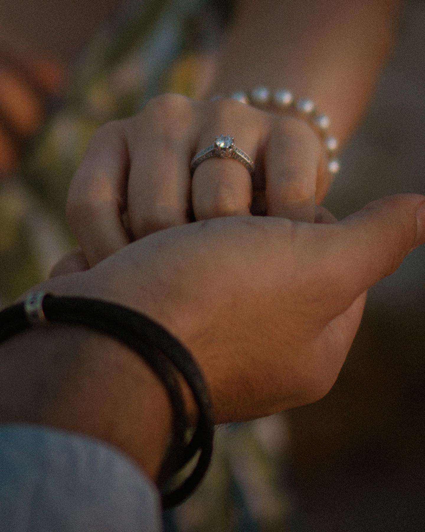 A man and woman share a tender moment as he holds her hand, featuring a stunning diamond ring that signifies their bond.