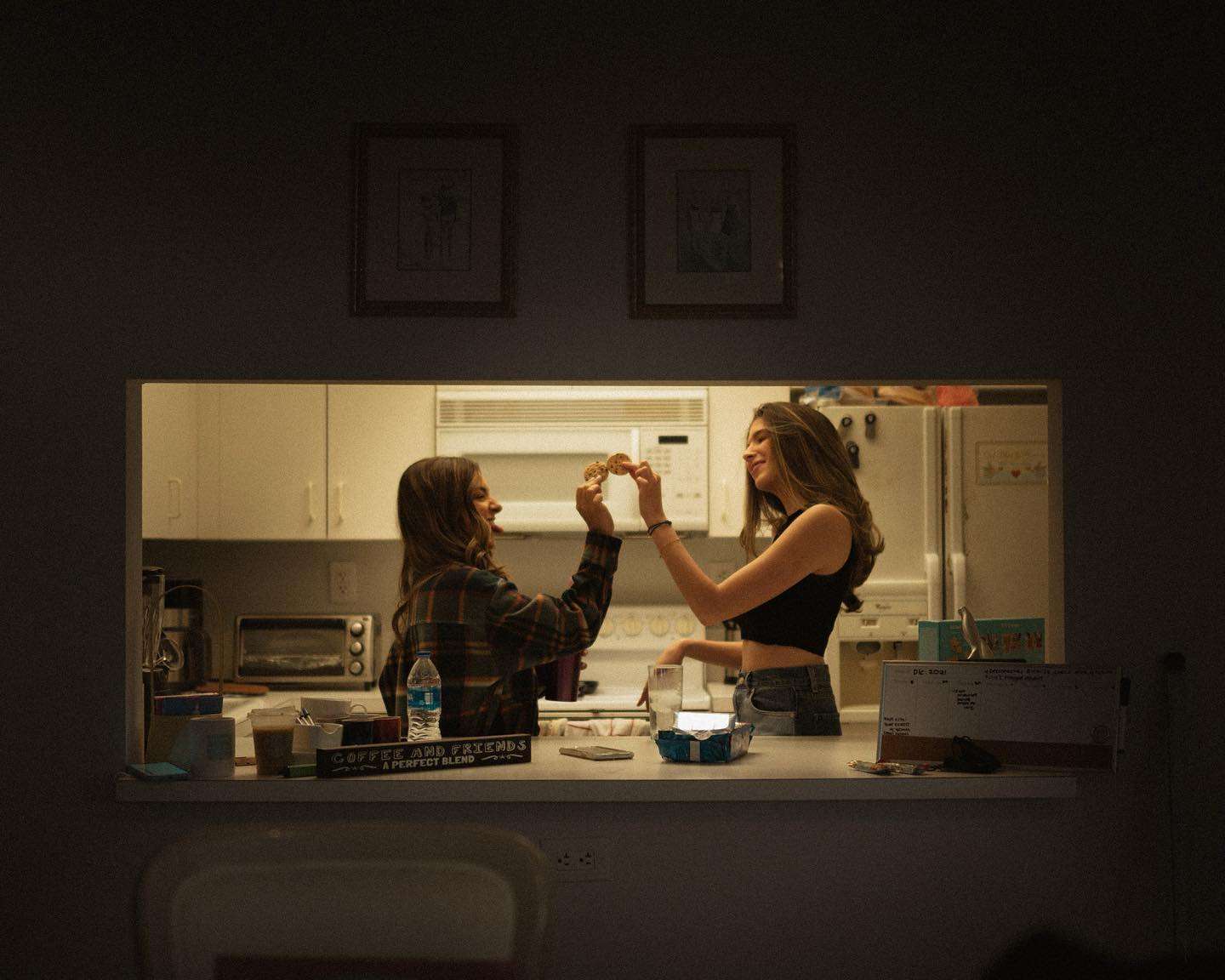 In a nighttime kitchen, two women are standing side by side, sharing a moment in the warm glow of the lights.