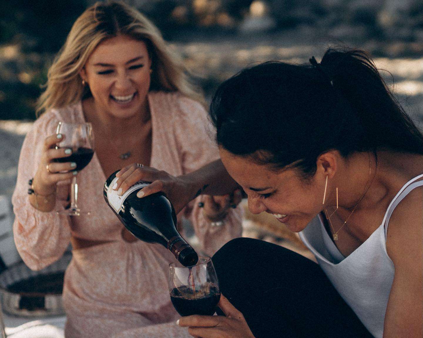 Two women seated at a picnic table, sharing a bottle of wine, immersed in conversation and the beauty of the outdoors.
