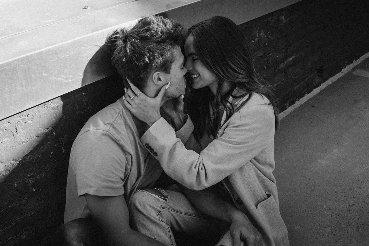 A couple sits closely on the ground, sharing a gentle kiss, embodying love and connection in a peaceful setting.
